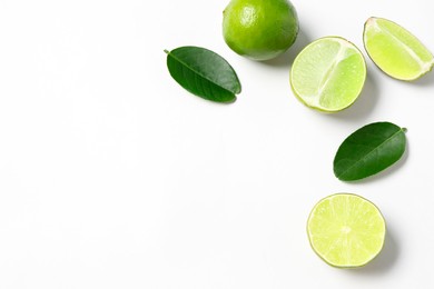 Photo of Fresh ripe limes and leaves on white background, flat lay. Space for text