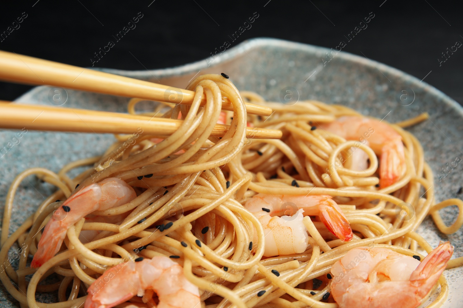 Photo of Chopsticks with tasty buckwheat noodles on black background, closeup