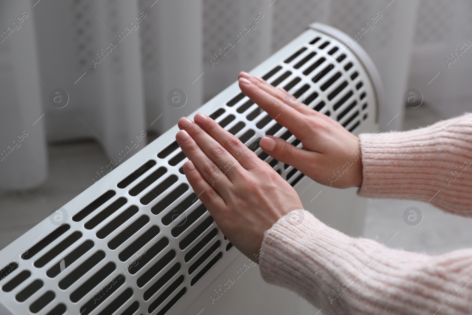 Photo of Woman warming hands near electric heater at home, closeup