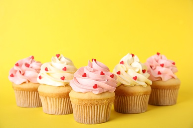 Photo of Tasty cupcakes with heart shaped sprinkles on yellow background. Valentine's Day celebration