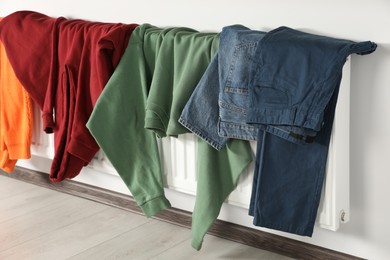 Photo of Clean clothes hanging on white radiator indoors