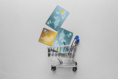 Photo of Small metal shopping cart with credit cards on light background, top view