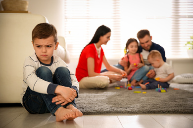 Unhappy little boy feeling jealous while parents spending time with other children at home
