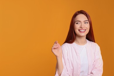 Beautiful woman with red dyed hair on orange background, space for text