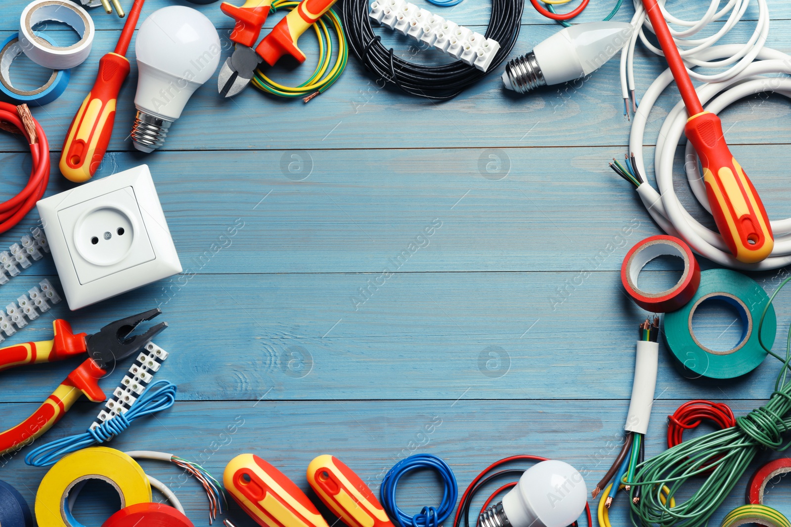 Photo of Frame of electrician's tools and accessories on light blue wooden table, flat lay. Space for text