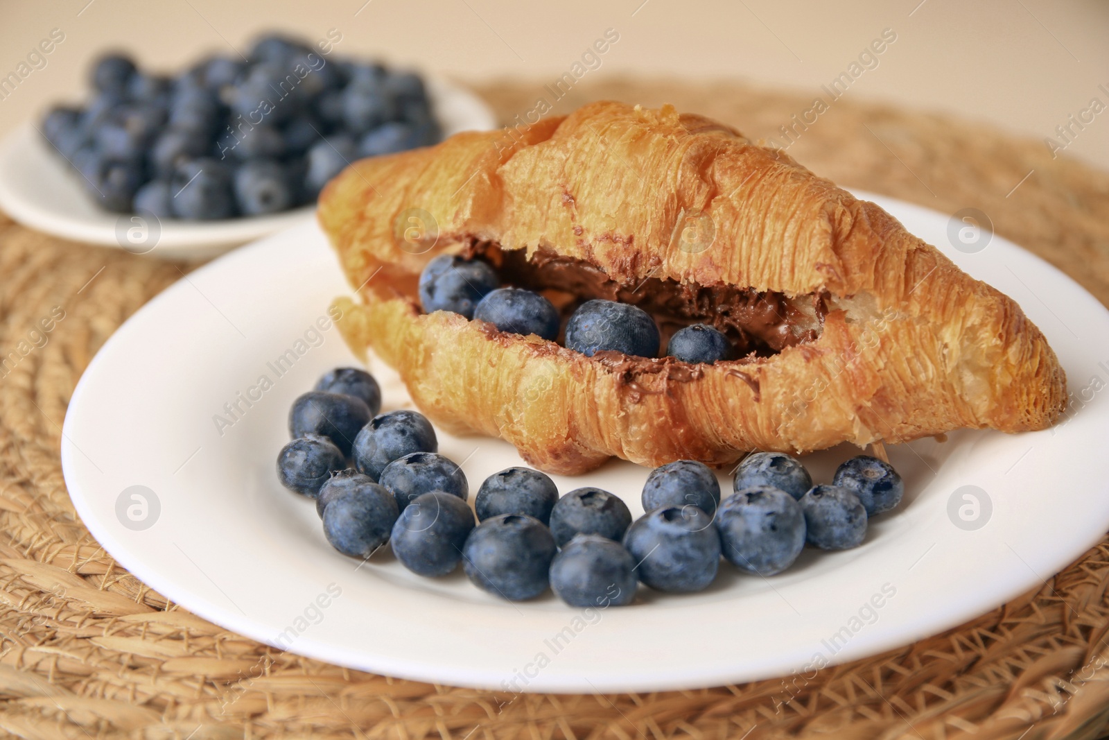 Photo of Tasty croissant with chocolate paste and blueberries on wicker mat