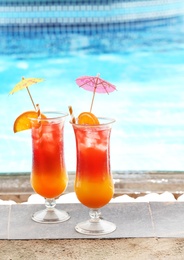 Glasses with tasty cocktails near swimming pool