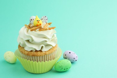 Tasty Easter cupcake with vanilla cream and candies on turquoise background, space for text