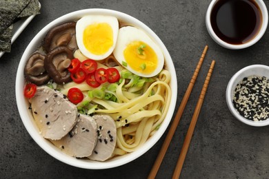 Photo of Delicious ramen with meat in bowl and ingredients on grey textured table, flat lay. Noodle soup