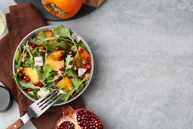 Tasty salad with persimmon, blue cheese, pomegranate and walnuts served on light grey table, flat lay. Space for text