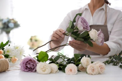 Photo of Florist making beautiful wedding bouquet at white table, closeup