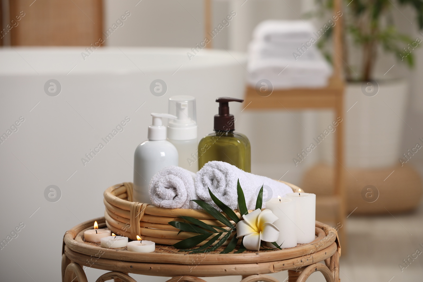 Photo of Spa products, burning candles, plumeria flower and tropical leaf on table in bathroom