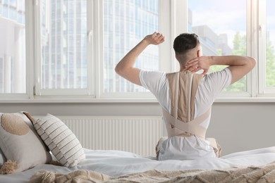 Man with orthopedic corset sitting in room, back view