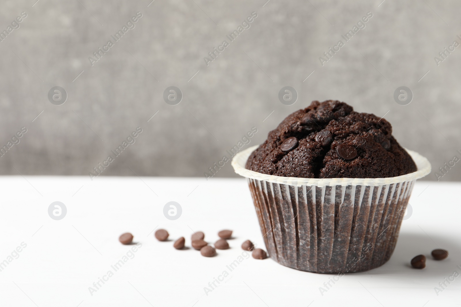 Photo of Tasty chocolate muffin on white table, space for text