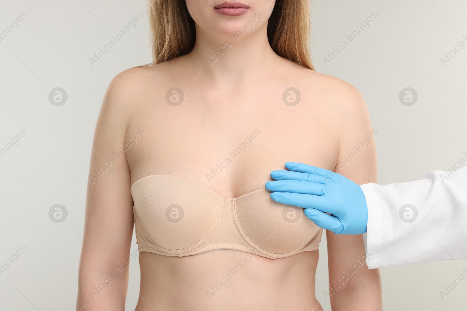 Photo of Mammologist checking woman's breast on light grey background, closeup