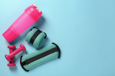 Photo of Turquoise weighting agents, dumbbells and shaker on light blue background, flat lay. Space for text