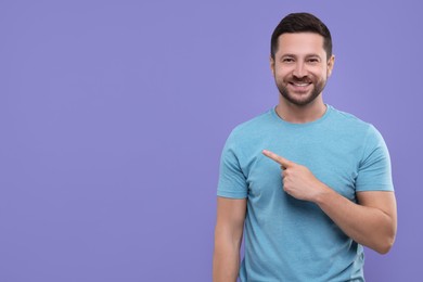 Photo of Special promotion. Smiling man pointing at something on purple background. Space for text