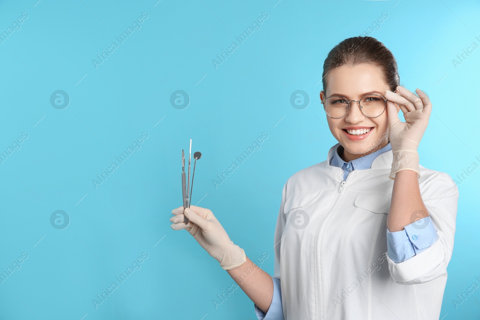 Photo of Female dentist holding professional tools on color background. Space for text