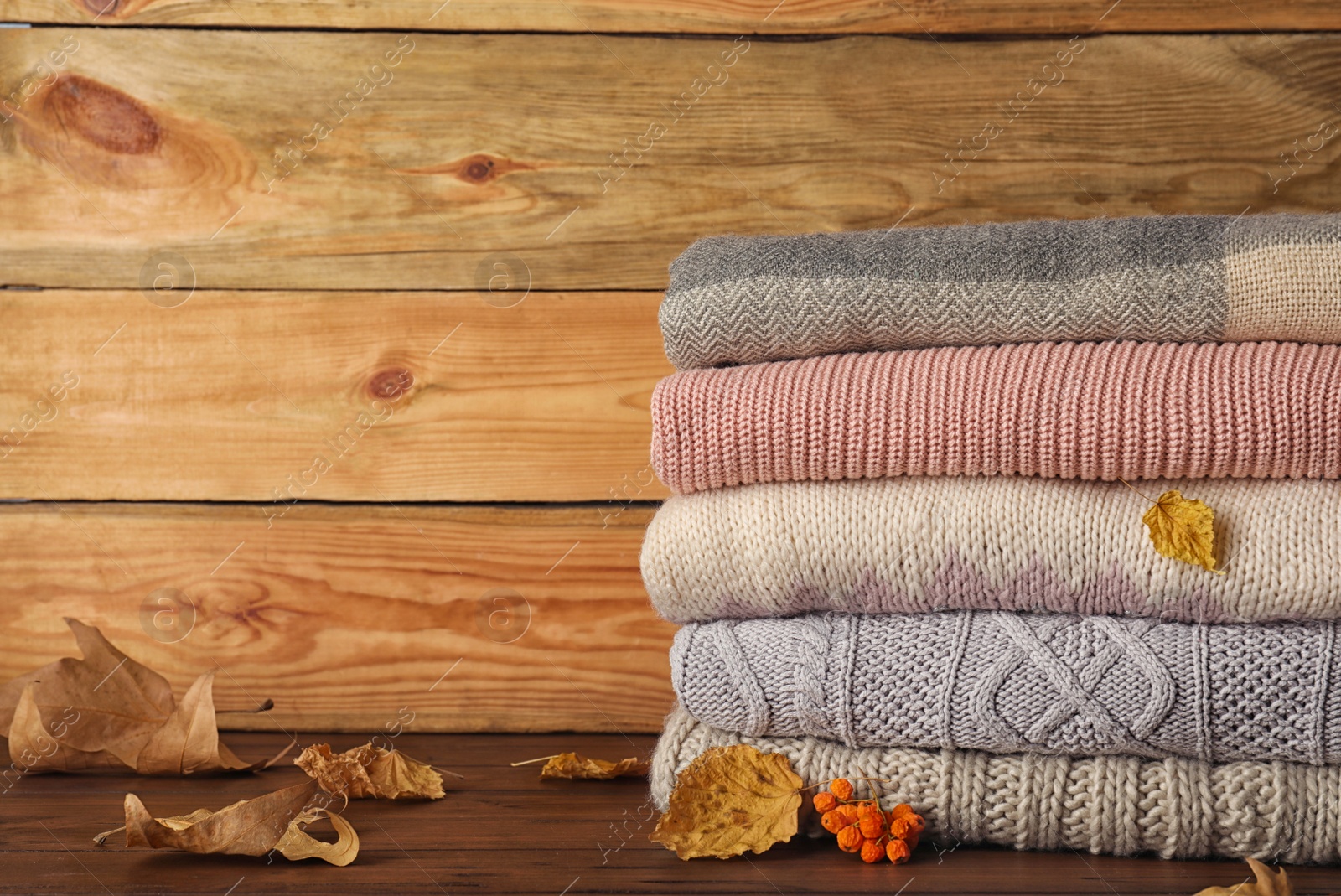 Photo of Stack of warm clothes with autumn leaves on wooden table. Space for text