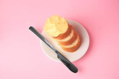 Photo of Slices of delicious baguette with butter and knife on pale pink background, above view