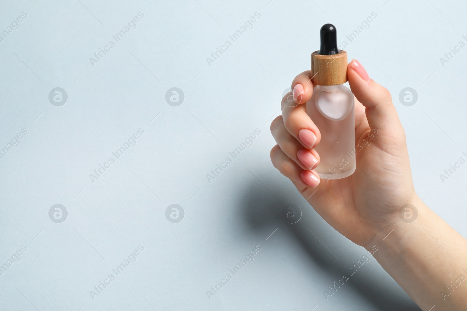 Photo of Woman holding bottle with serum on light blue background, closeup. Space for text