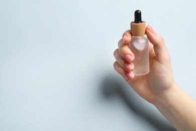 Woman holding bottle with serum on light blue background, closeup. Space for text