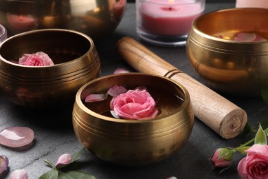 Photo of Tibetan singing bowls with water, beautiful rose flowers and mallet on gray table, closeup