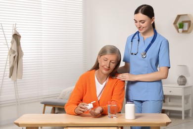 Photo of Senior woman with bottle of pills and young healthcare worker indoors. Space for text
