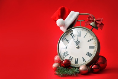 Alarm clock and festive decor on red background, space for text. New Year countdown