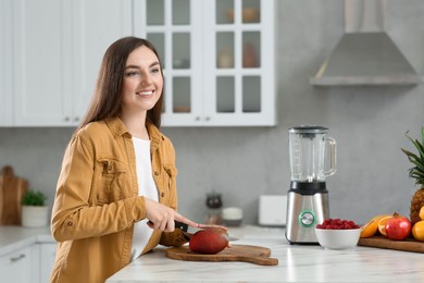 Woman preparing mango for tasty smoothie at white marble table in kitchen