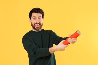 Emotional man with party popper on yellow background