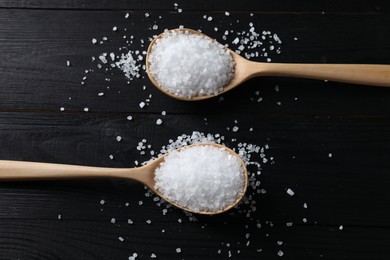 Photo of Organic salt in spoons on black wooden table, top view