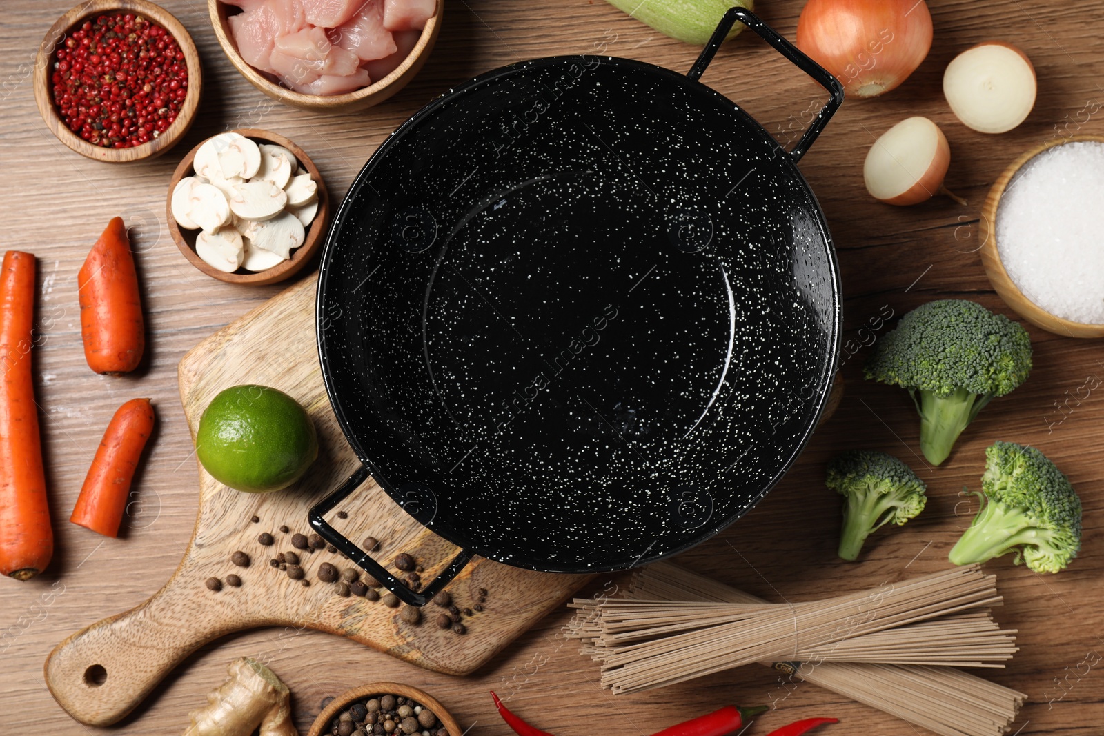 Photo of Empty iron wok surrounded by raw ingredients on wooden table, flat lay