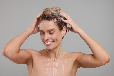 Beautiful happy woman washing hair on light grey background