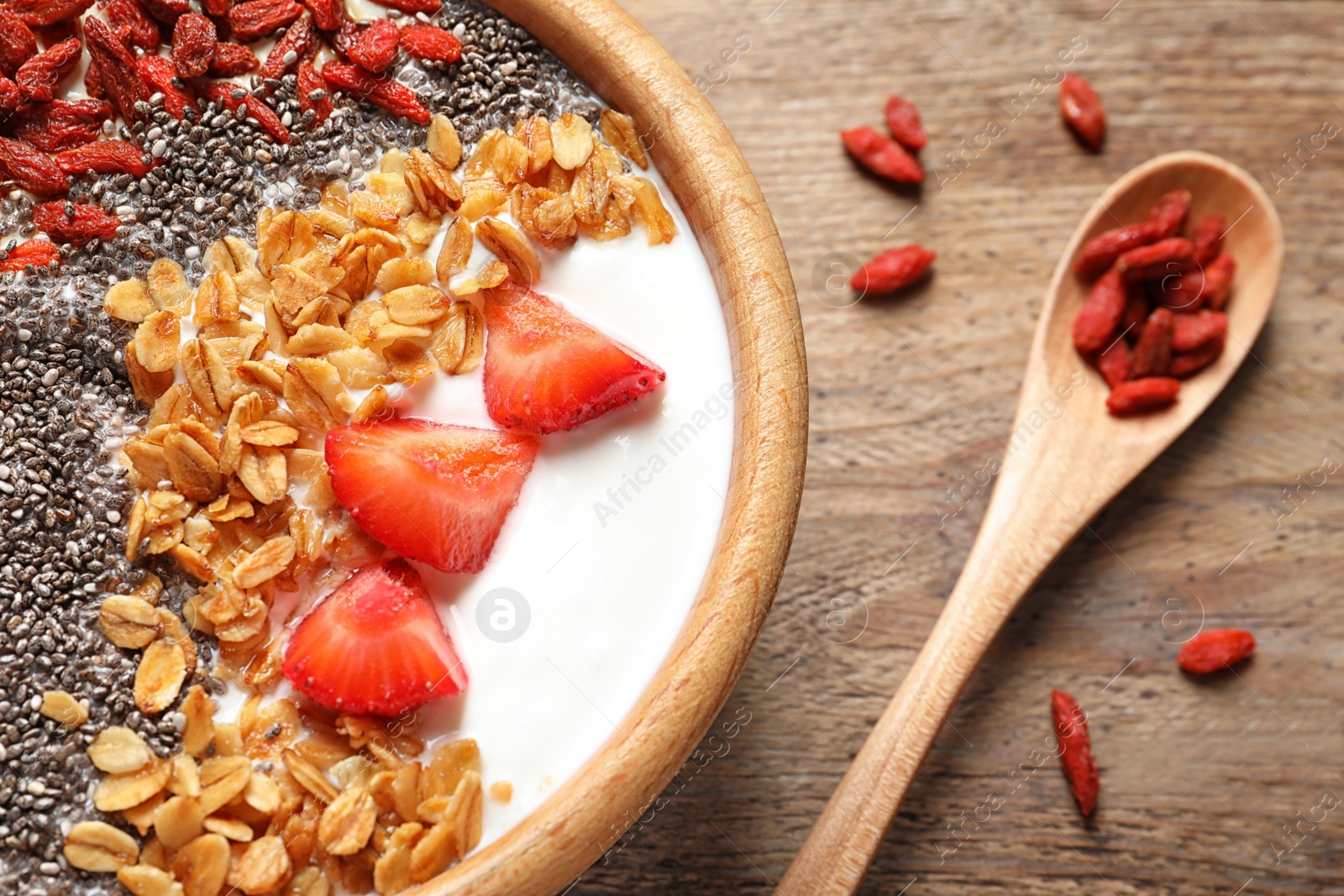 Photo of Smoothie bowl with goji berries and spoon on wooden table, closeup