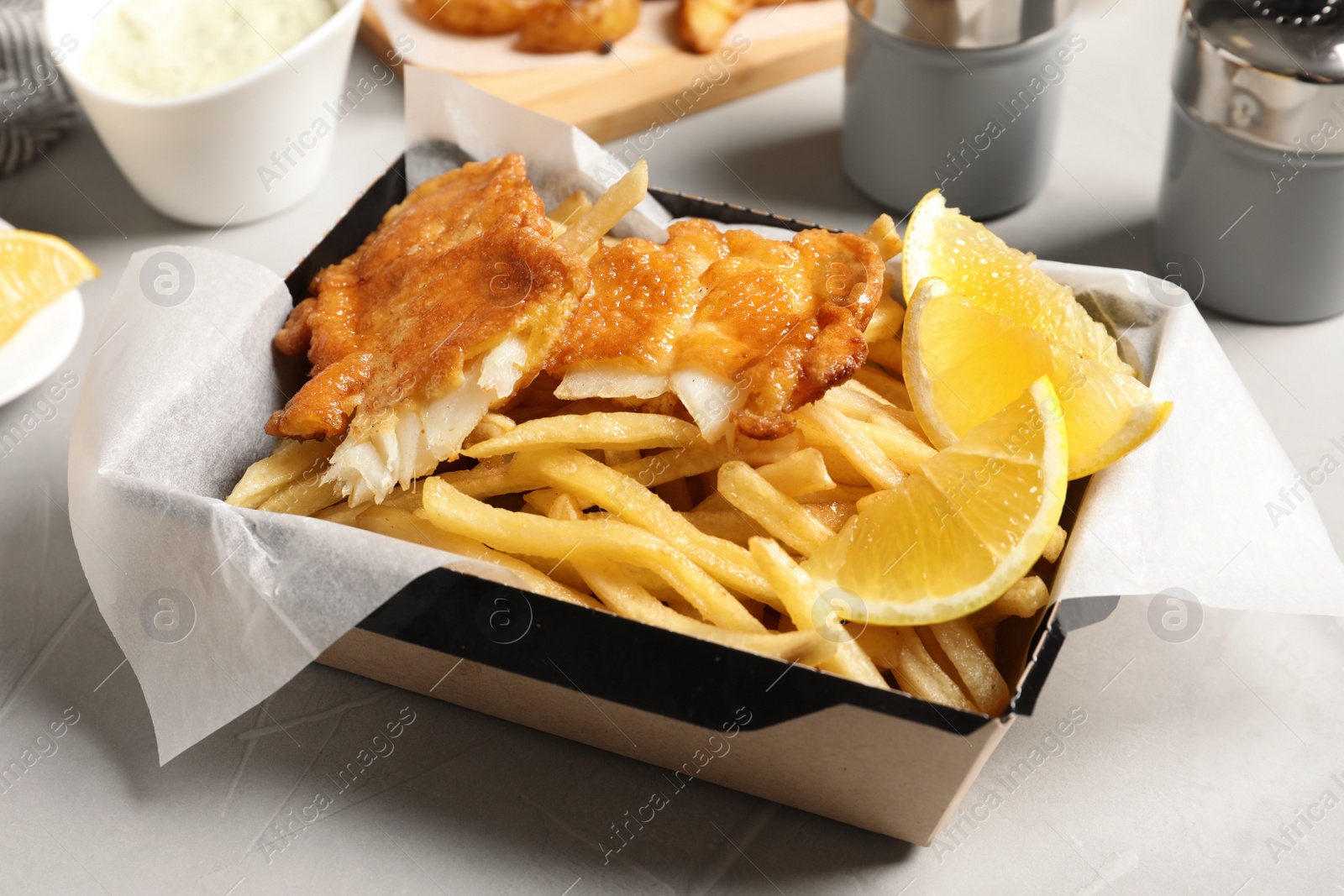 Photo of Container with British traditional fish and potato chips on table