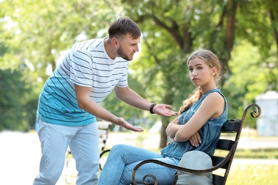 Photo of Young couple arguing while sitting on bench in park. Problems in relationship