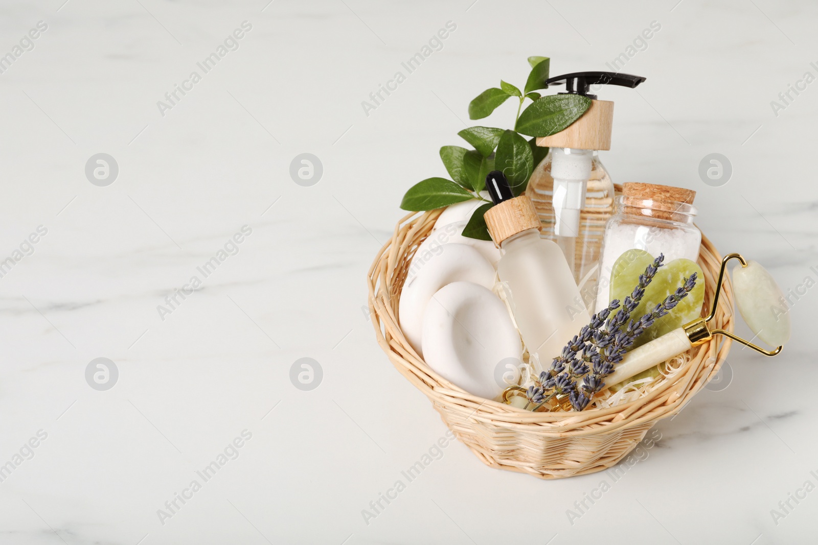 Photo of Spa gift set in wicker basket on white marble table. Space for text