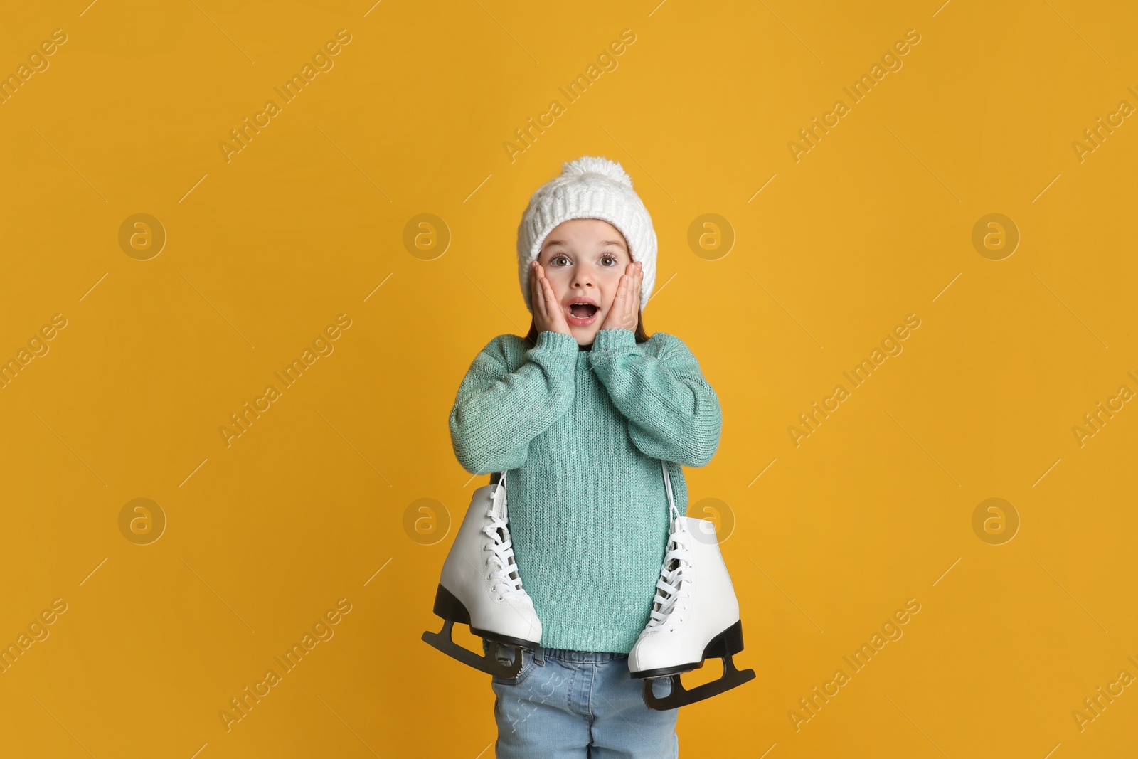 Photo of Excited little girl in turquoise knitted sweater with skates on yellow background