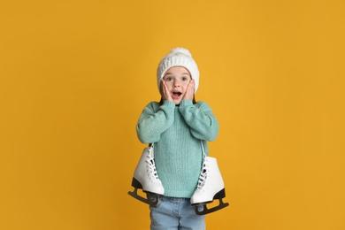 Photo of Excited little girl in turquoise knitted sweater with skates on yellow background