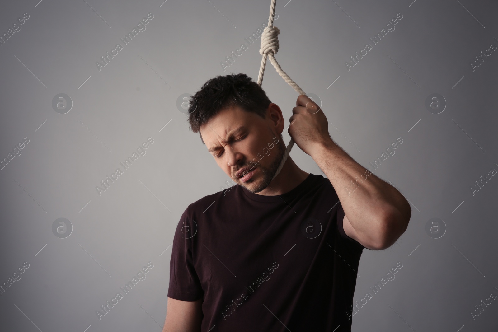 Photo of Depressed man with rope noose on neck against light grey background