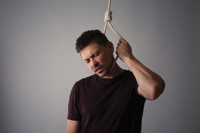 Depressed man with rope noose on neck against light grey background