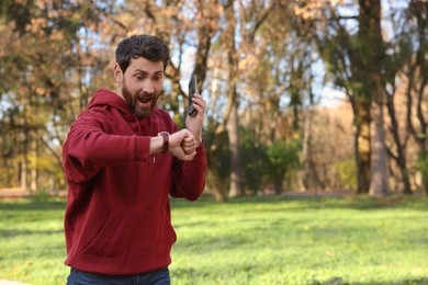 Photo of Emotional man talking by smartphone and checking time on watch in park, space for text. Being late concept