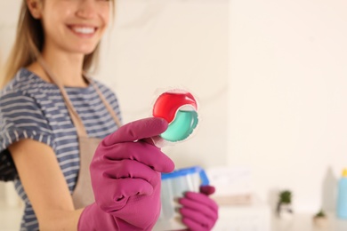 Photo of Happy woman holding laundry detergent capsule indoors, closeup