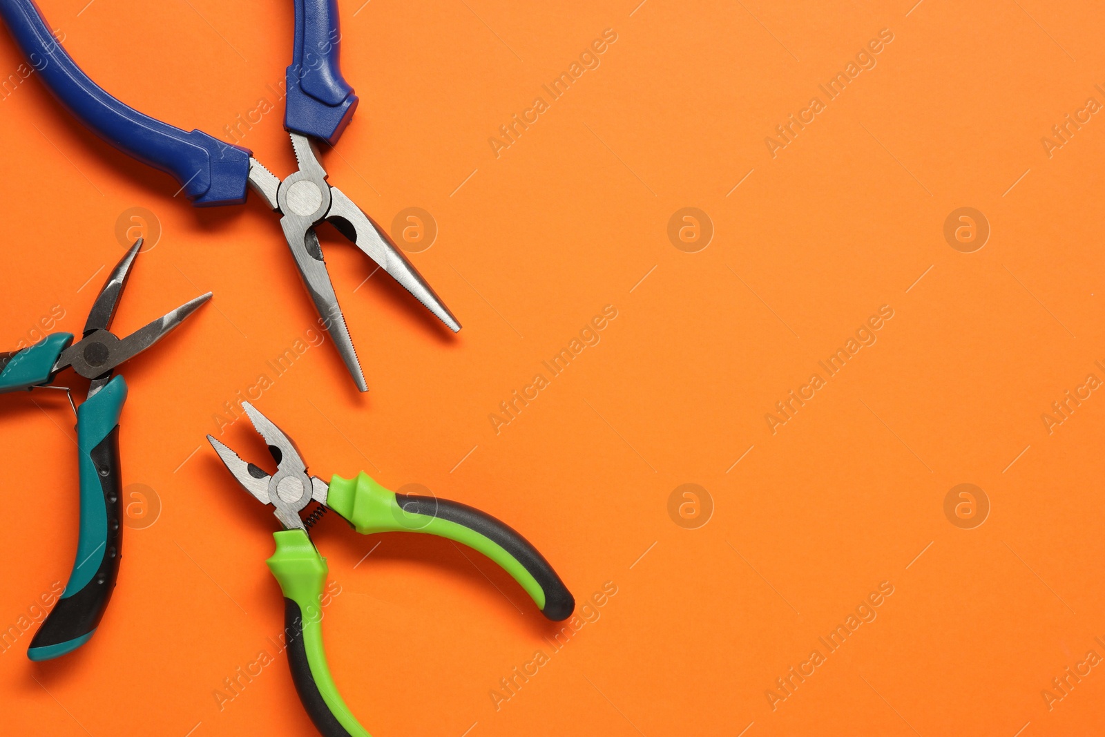 Photo of Different pliers on orange background, flat lay. Space for text