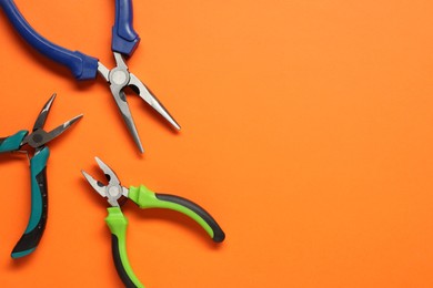 Different pliers on orange background, flat lay. Space for text