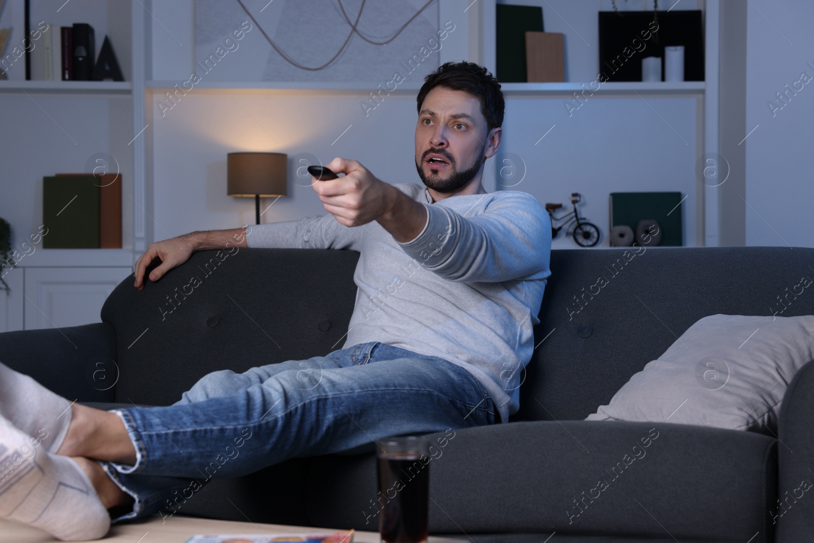 Photo of Man changing TV channels with remote control on sofa at home