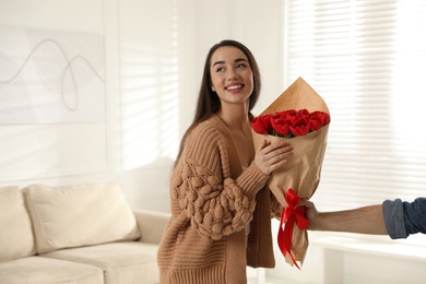 Photo of Happy woman receiving red tulip bouquet from man at home, space for text. 8th of March celebration