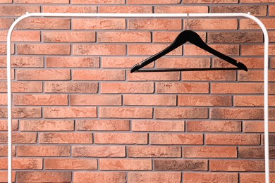 Black clothes hanger on rack near red brick wall. Space for text