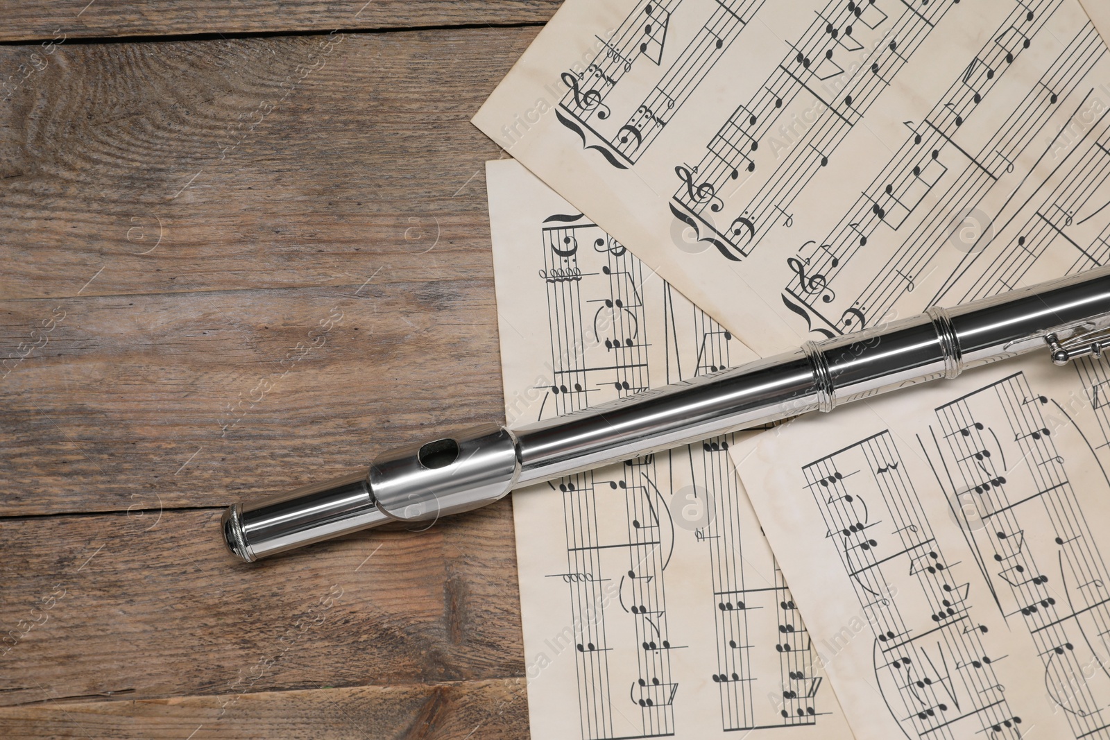 Photo of Sheets with musical notes and flute on wooden table, flat lay. Space for text